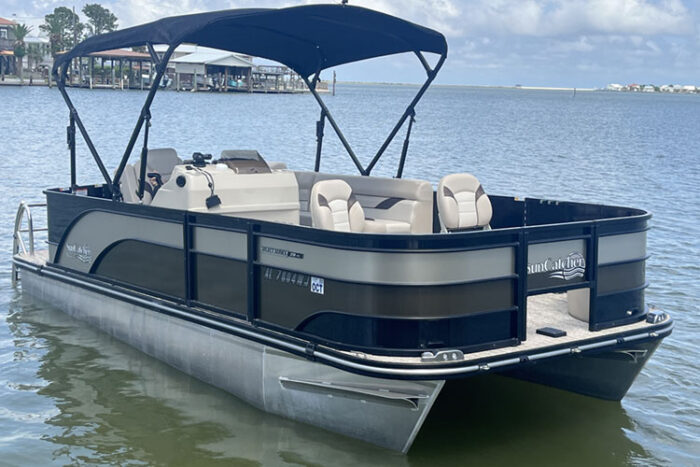 Pontoon boat with a black canopy floating on calm water near a dock