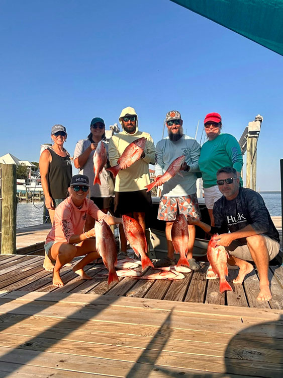 Group of anglers posing on a dock with several red fish after a successful catch
