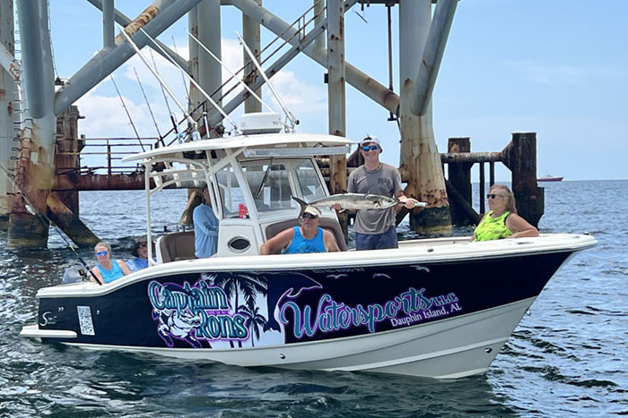 Captain Ron's Watersports boat with four passengers under a pier, holding up a large fish