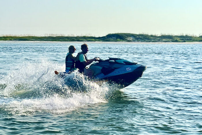 Two people riding a jet ski across calm water with spray behind them