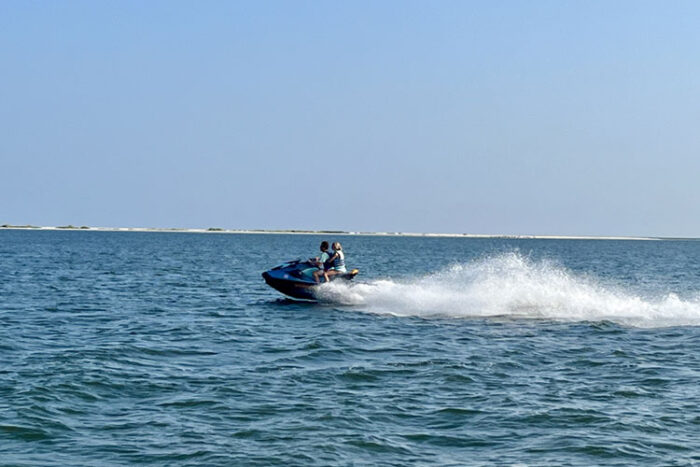 Two riders on a jet ski speeding across open water and kicking up spray