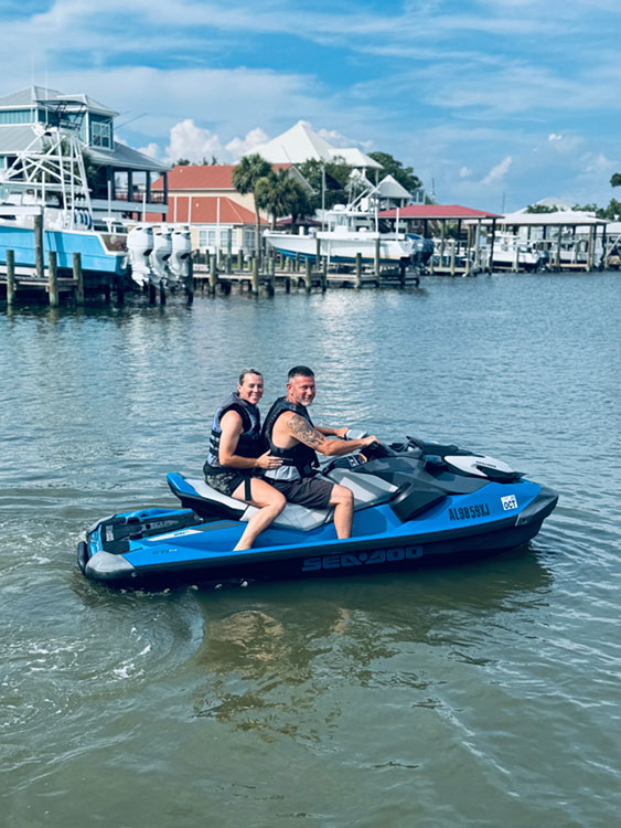 Couple riding a blue Sea-Doo jet ski on calm water near a marina