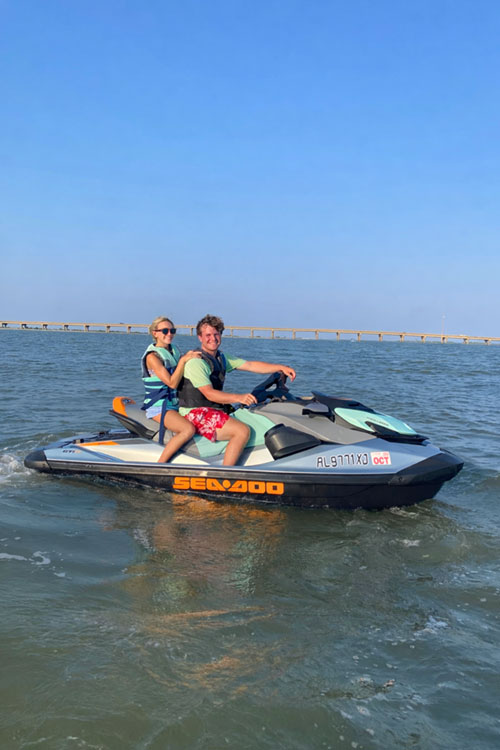 Two people riding a Sea-Doo jet ski on calm water under a clear blue sky